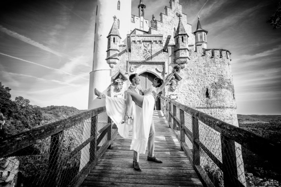 Zwei Frauen in weißen Kleidern stehen auf einer Holzbrücke vor einem Schloss.