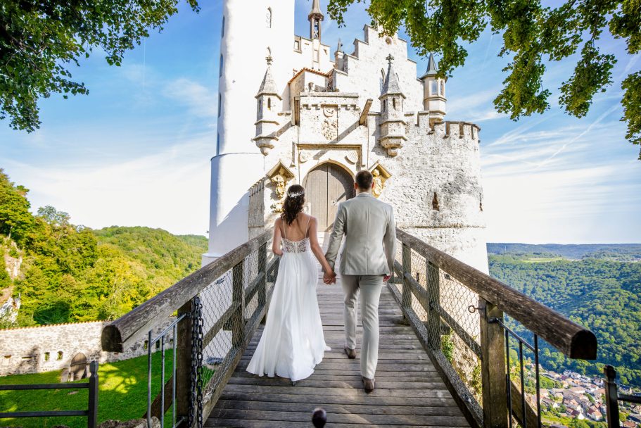 Ein frisch vermähltes Paar geht über die Brücke zu einer Burg in malerischer Landschaft.