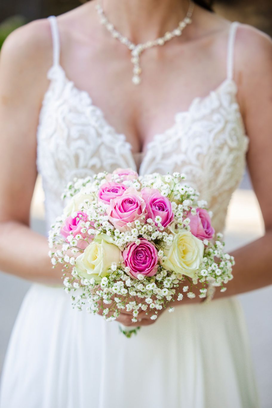 Braut hält einen Strauß aus rosa und weißen Rosen mit Schleierkraut.
