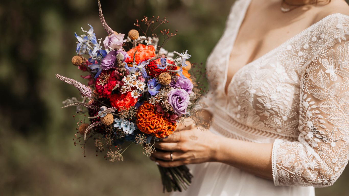 Braut hält einen bunten Blumenstrauß mit verschiedenen floralen Akzenten.