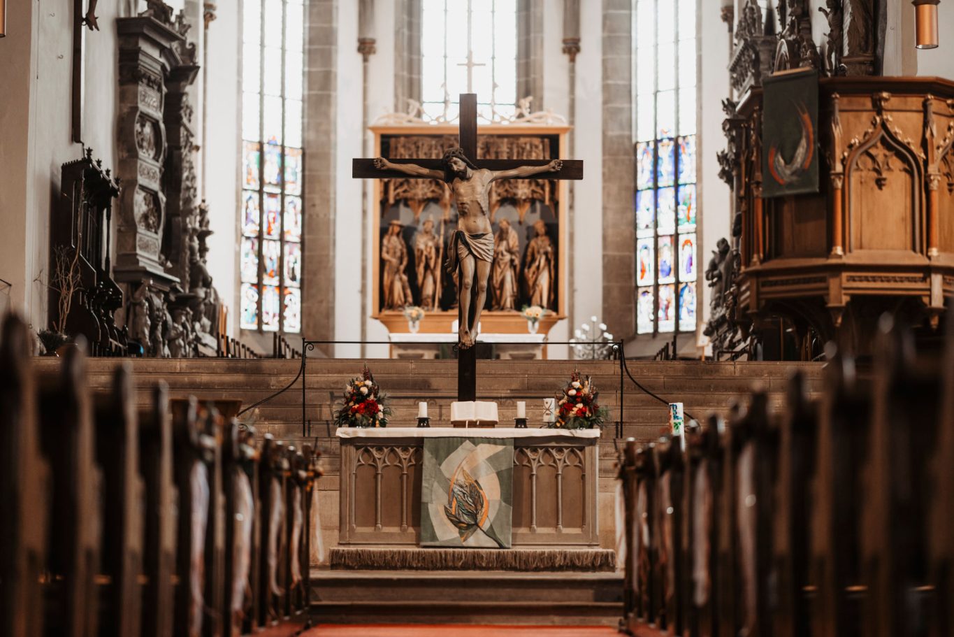 Stiftskirche Öhringen mit Altar, Kreuz und bunten Fenstern.