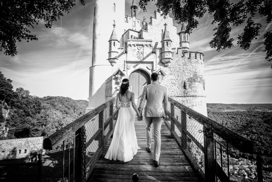 Ein Brautpaar geht Hand in Hand über eine Brücke zu einem beeindruckenden Schloss.