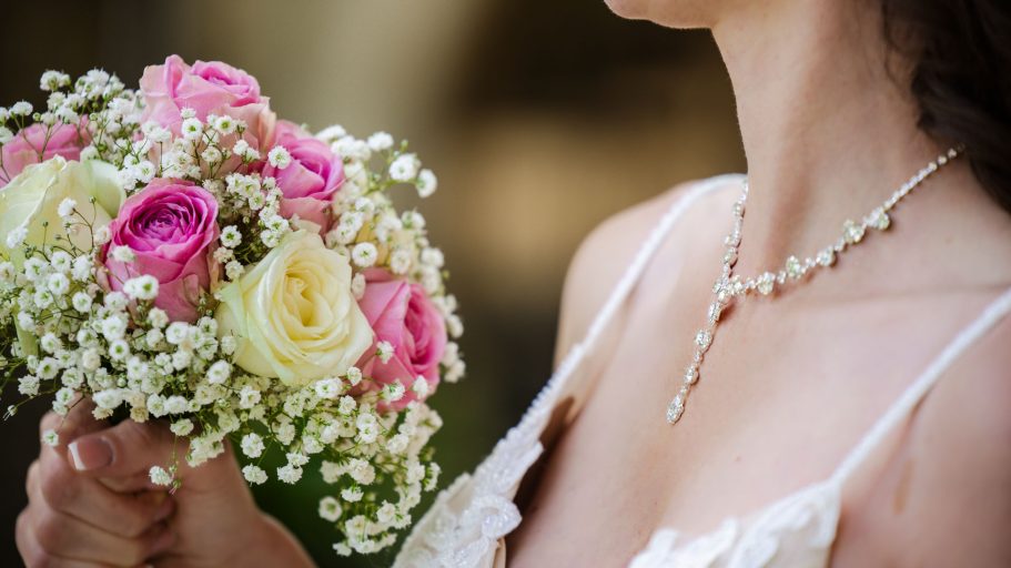 Braut mit einem Blumenstrauß aus rosa und weißen Rosen, trägt eine elegante Halskette.
