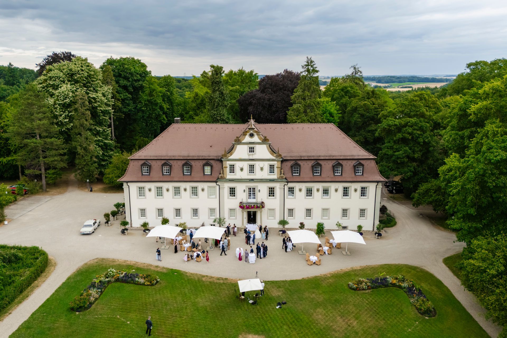 Das historische Jagdschloss Gebäude umgeben von Bäumen, mit Hochzeitsgästen im Freien.