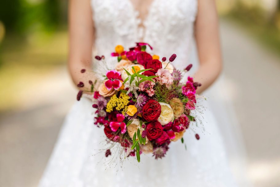 Braut hält einen bunten Blumenstrauß mit roten, rosa und gelben Blüten.