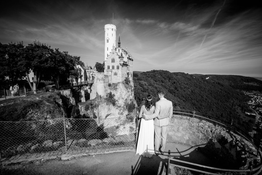 Hochzeitspaar vor einer Burg auf einem Felsen mit malerischer Aussicht.