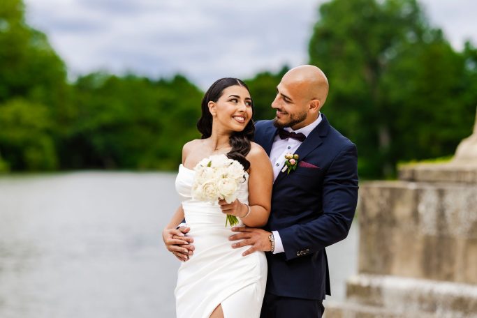 Paar in formeller Hochzeitskleidung lächelt verliebt am See.