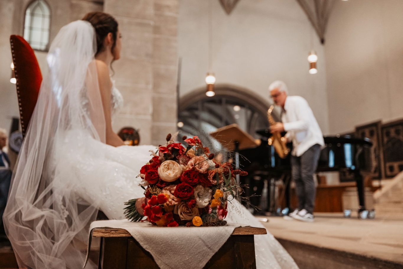 Braut mit einem Blumenstrauß sitzt, während ein Saxophonist im Hintergrund spielt.