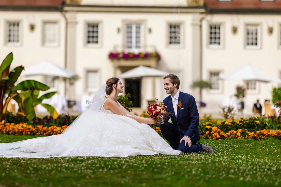 Braut und Bräutigam posieren im Garten vor den eleganten Gebäude von Schlosshotel Friedrichsruhe.