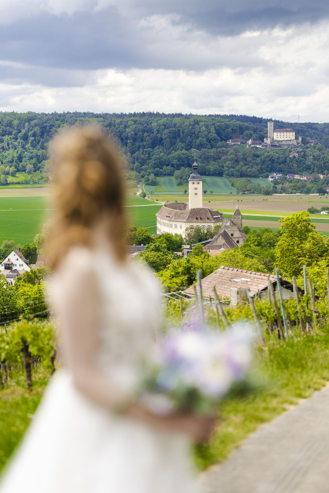 Braut mit Blumenstrauß, unscharf im Vordergrund, Blick auf Schloß Horneck in Gundelsheim.