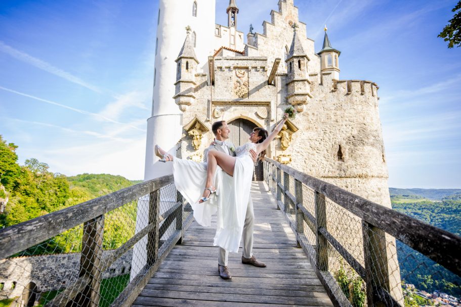 Paar in eleganter Kleidung tanzt auf einer Holzbrücke vor einem Schloss.
