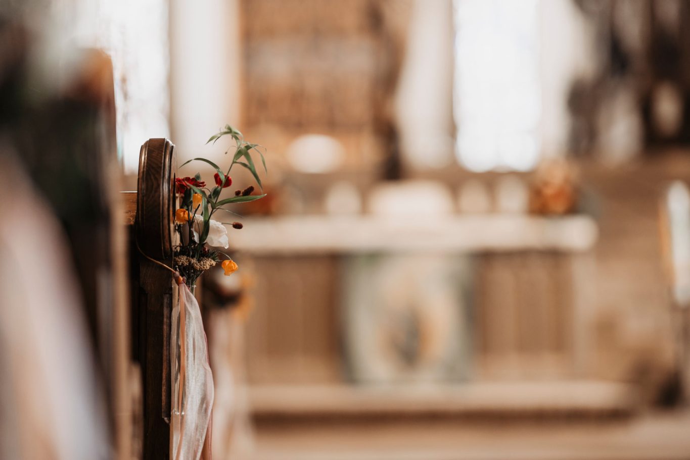 Dekorative Blumenarrangements auf einer Kirchenbank im Hintergrund ein Altar.